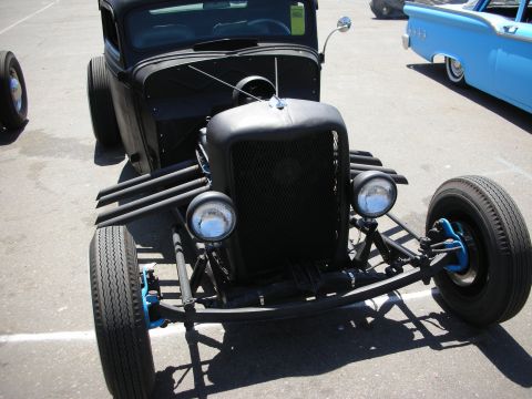 1998 Ford Crown Victoria - Front view of a black rat-rod truck with a mesh grille, twin round headlights, blue accents, and a fat front tire in a paved lot.