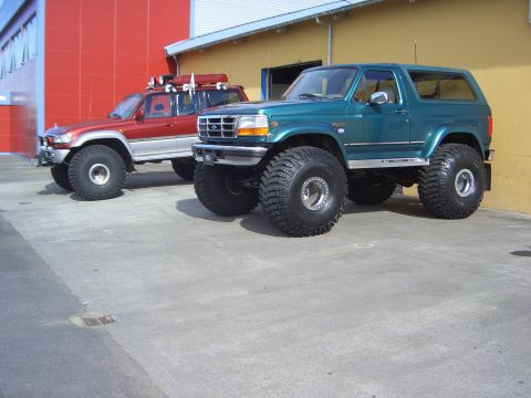 1996 Ford Bronco - A lifted 1996 Ford Bronco with oversized tires is parked on pavement next to another modified SUV.
