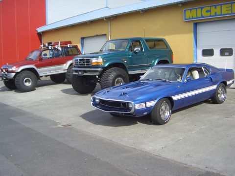 1996 Ford Bronco - Three modified vehicles, including a blue 1969 Mustang Mach 1, are parked outside a building.