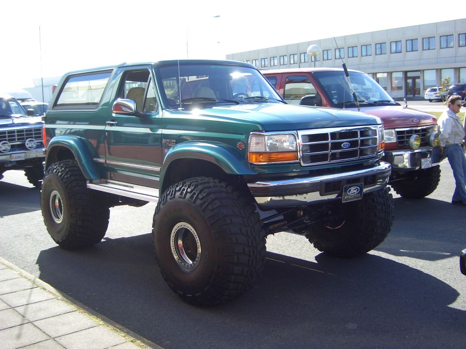 Lifted teal Ford Bronco on huge off-road tires in a parking lot