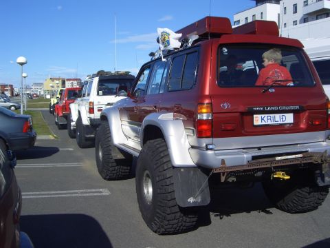 1996 Ford Bronco - A red Toyota Land Cruiser is parked in a lot, showing its lifted suspension and large off-road tires.