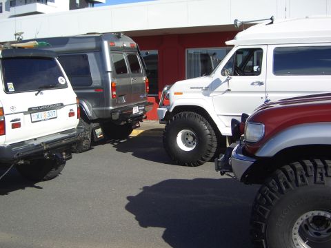 1996 Ford Bronco - Multiple off-road vehicles are parked together in a lot, with a red vehicle partially visible in the foreground.