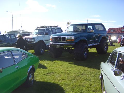 1996 Ford Bronco - A lifted green Ford Bronco is parked on a grassy field alongside other vehicles under a partly cloudy sky.