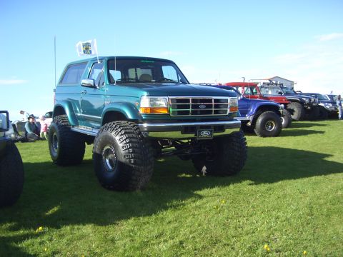 1996 Ford Bronco - A lifted green 1996 Ford Bronco is parked on a grassy field with other vehicles in the background under a clear blue sky.