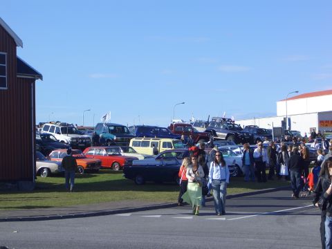 1996 Ford Bronco - A crowd gathers around a diverse collection of vehicles parked on a grassy lot.