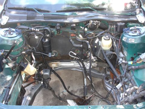 1993 Ford Taurus - Engine bay of a green car with the engine removed, exposing the subframe and various hoses.