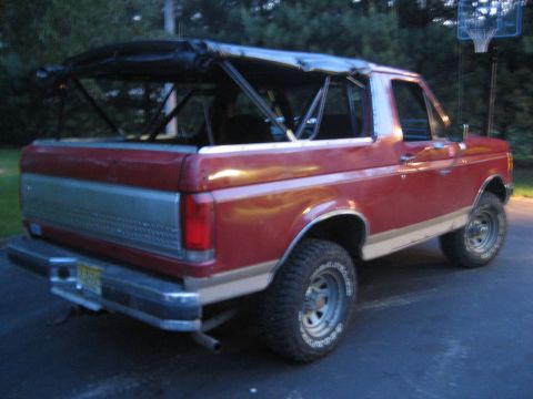 1990 Ford Bronco - This red Ford Bronco has a black soft top and roll cage, viewed from the rear-right.