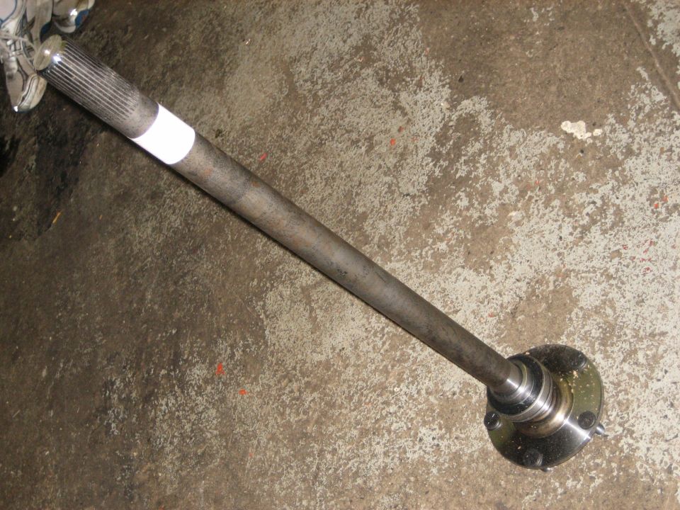 Removed rear axle shaft with splined end and hub flange with wheel studs on concrete floor