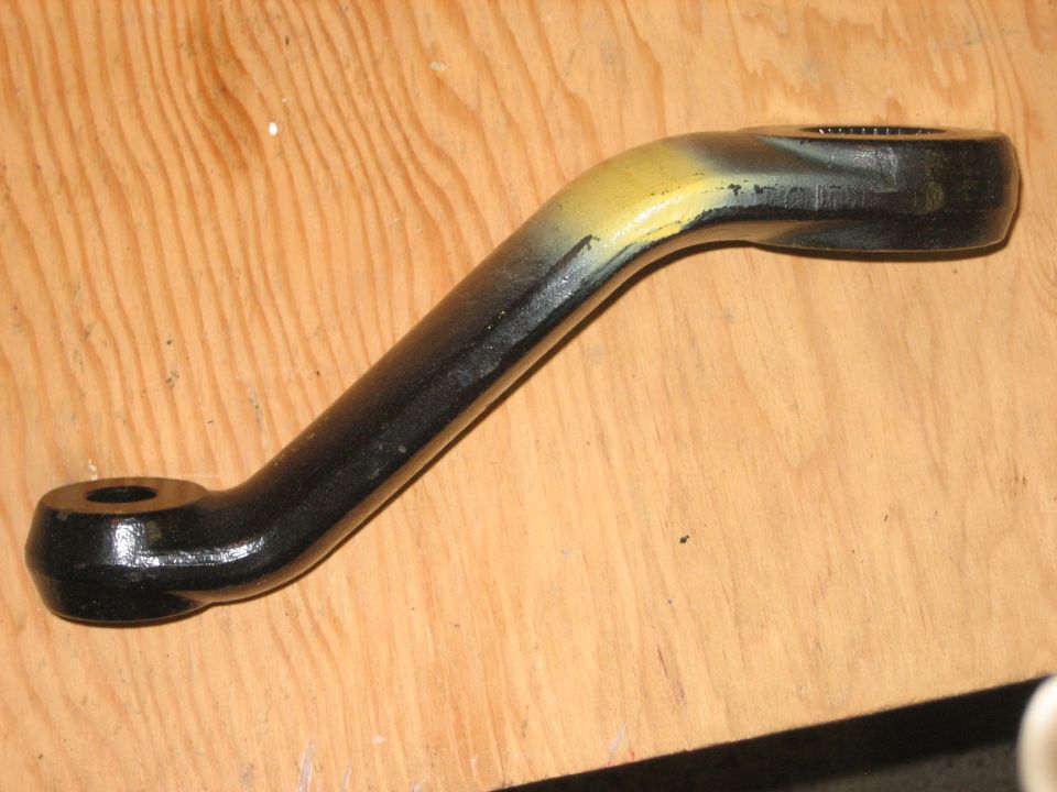 Black forged steering arm with yellow markings lying on plywood workbench