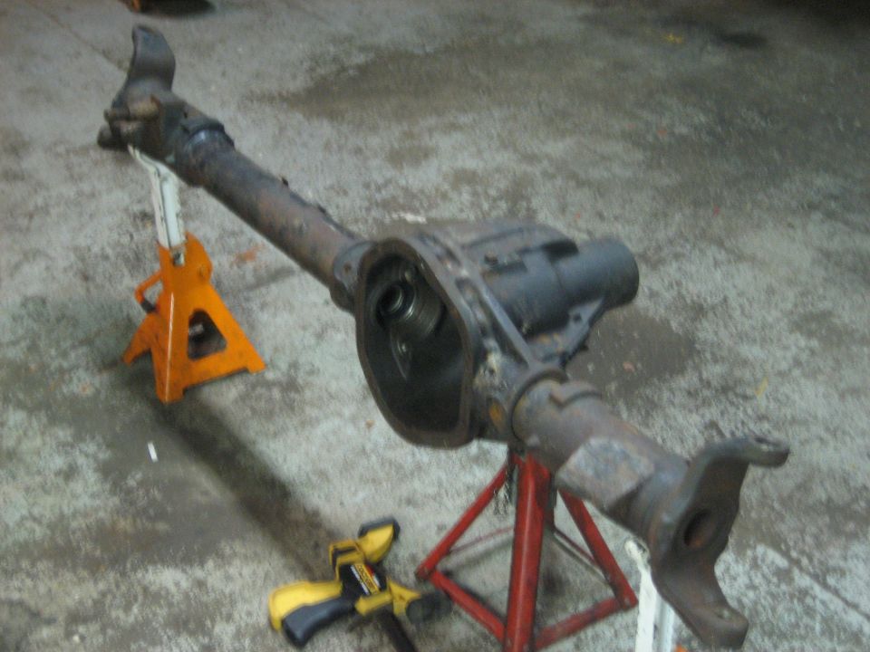 Removed rusty solid axle with open differential housing supported on two jack stands on a garage floor