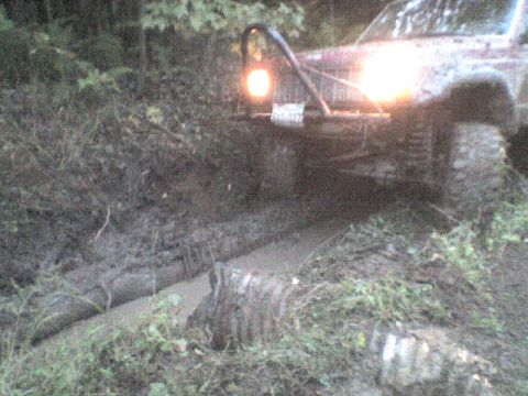 1984 Ford Bronco - This off-road vehicle appears to be stuck in a muddy ditch, with its headlights illuminating the challenging terrain.