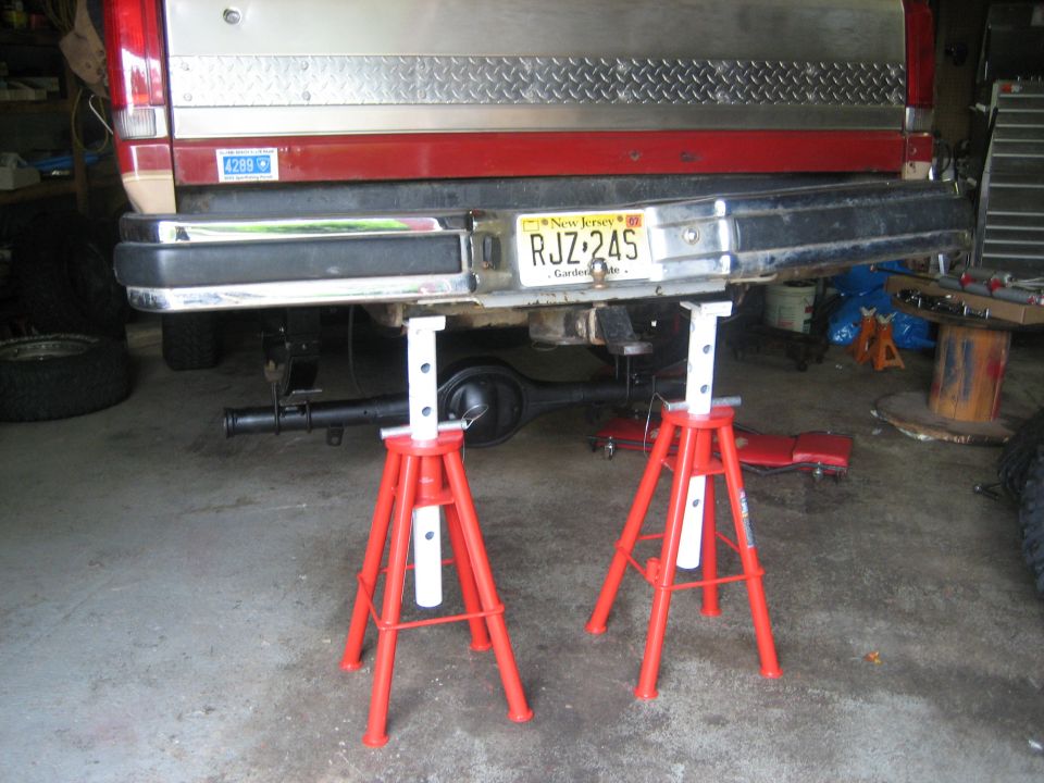 Red Ford Bronco on tall jack stands in a garage with rear axle removed