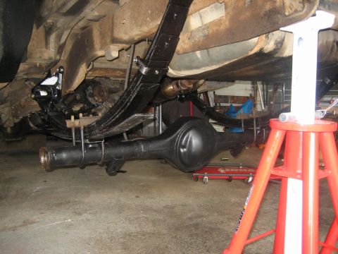 1990 Ford Bronco - Low-angle underbody shot of a freshly painted black rear axle housing with the brake drums and axle shafts pulled, sitting under a vehicle…