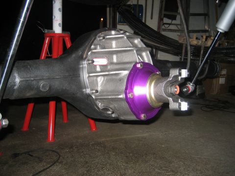 1990 Ford Bronco - Close-up under a lifted truck of a rear axle center section with an aluminum third-member/differential cover, fitted with a purple anodized…