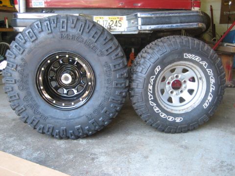 1990 Ford Bronco - Tire size comparison in a garage: a tall Mickey Thompson Baja Claw Radial mud tire on a black beadlock-style steel wheel stands next to a n…