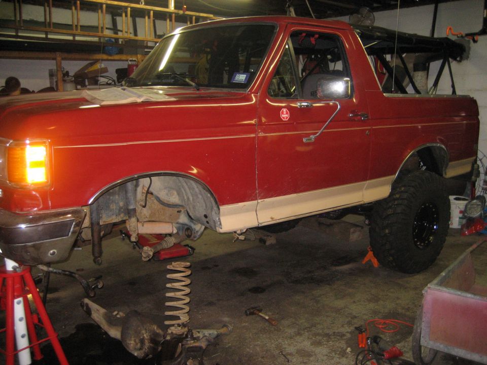 Red Ford Bronco on jack stands with front axle and coil spring removed