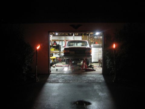1990 Ford Bronco - A red 1990 Ford Bronco is elevated on jack stands inside a garage, illuminated by torches outside.