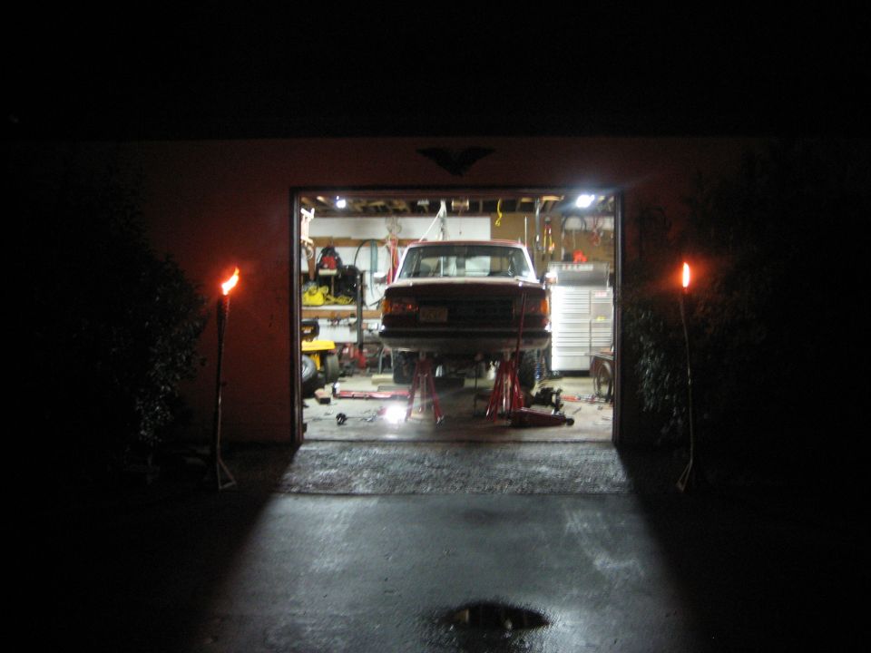 Red 1990 Ford Bronco on jack stands in garage, rear view