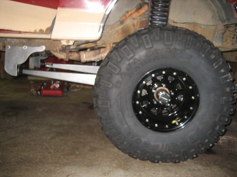 1990 Ford Bronco - Ground-level shot of a red-and-tan lifted 4x4's front corner in a garage, showing a Mickey Thompson Baja Claw Radial mud tire on a black si…