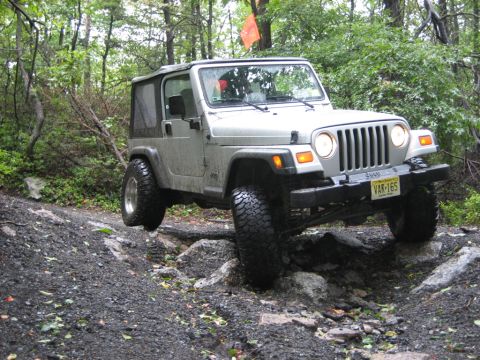 2002 Jeep Wrangler - A silver 2002 Jeep Wrangler navigates a challenging rocky path in a wooded area.