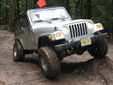 2002 Jeep Wrangler - Silver 2002 Jeep Wrangler navigating a muddy trail with one wheel lifted.