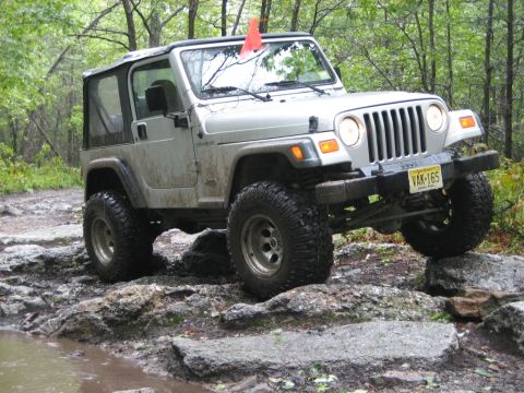 2002 Jeep Wrangler - A Jeep Wrangler navigates a rocky off-road trail with a soft top and an orange flag on the antenna.