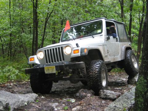 2002 Jeep Wrangler - A silver Jeep Wrangler navigates a challenging rocky trail in a wooded area.
