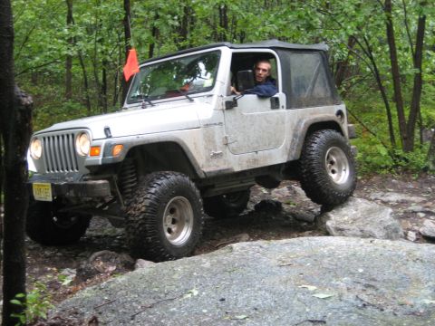 2002 Jeep Wrangler - A silver 2002 Jeep Wrangler tackles a challenging rocky trail with a driver behind the wheel.