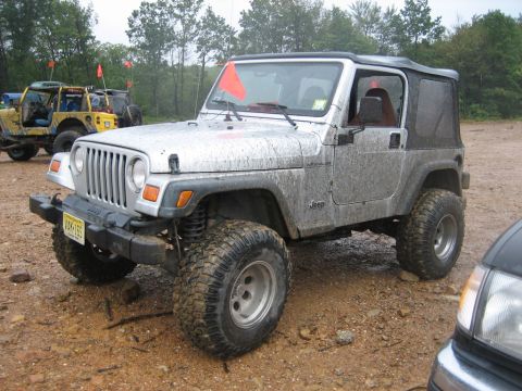 2002 Jeep Wrangler - Muddy 2002 Jeep Wrangler parked on dirt with other vehicles in the background.