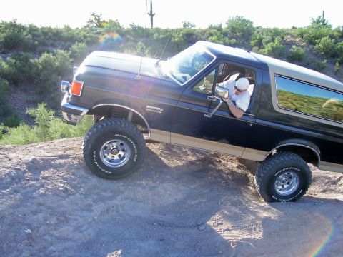 1991 Ford Bronco - A driver navigates a dark blue 1991 Ford Bronco over a rough, rocky incline.