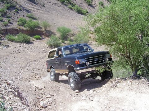 1991 Ford Bronco - This 1991 Ford Bronco navigates a , dusty trail with a prominent lift kit and off-road tires.
