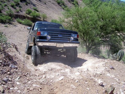 1991 Ford Bronco - This lifted Ford Bronco navigates a challenging off-road path with steep inclines and loose terrain.