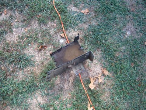 1988 Ford Bronco - A metal bracket, possibly a vehicle part, lies on a grassy area with an orange cord nearby.