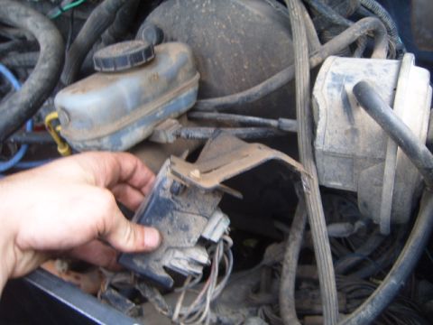 1988 Ford Bronco - Close-up of an engine bay, focusing on a hand holding a part near the brake fluid reservoir.