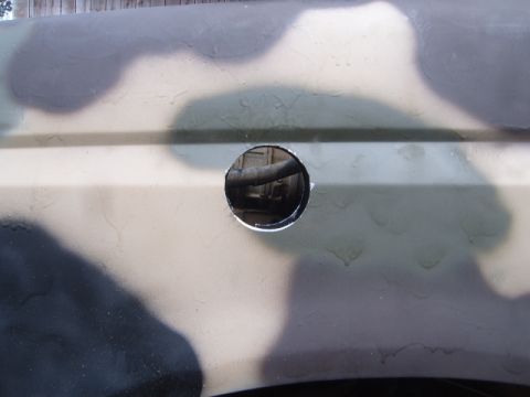 1988 Ford Bronco - A close-up view of a vehicle's fender, painted in a camouflage pattern, with a hole cut into it.