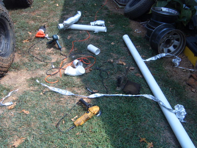 PVC pipe, heat gun and yellow angle grinder laid out on grass beside off-road tires.