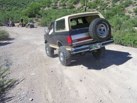1991 Ford Bronco - A lifted Ford Bronco drives on a dusty trail with several ATVs following behind.