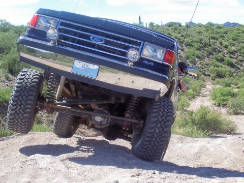 1991 Ford Bronco - A black Ford Bronco navigates a steep, rocky incline on a desert trail.