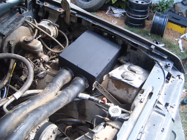 Engine bay with front end removed, black box component and hoses visible