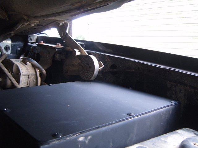 Engine bay interior with black flat cover panel and firewall-mounted component