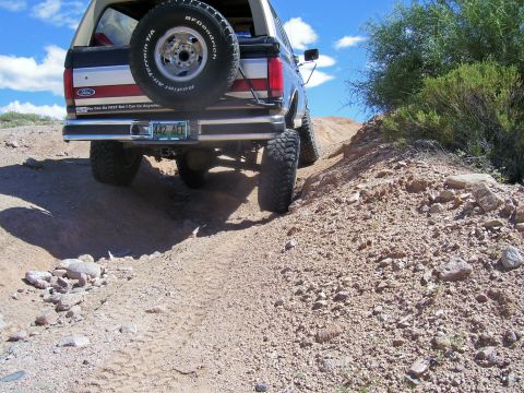 1991 Ford Bronco - A lifted Ford Bronco navigates a rocky dirt path under a clear blue sky.