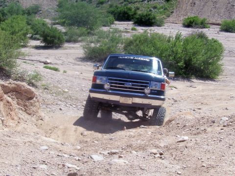 1991 Ford Bronco - This Ford truck is navigating a rough, dusty trail with sparse vegetation.
