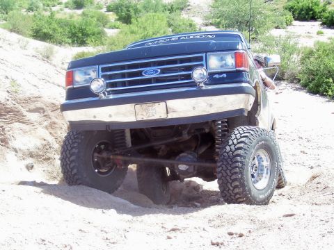 1991 Ford Bronco - This lifted Ford Bronco navigates a sandy, off-road terrain with its front end angled towards the camera.