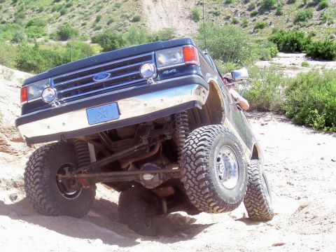 1991 Ford Bronco - This modified Ford Bronco is navigating a steep, off-road incline with one wheel lifted.