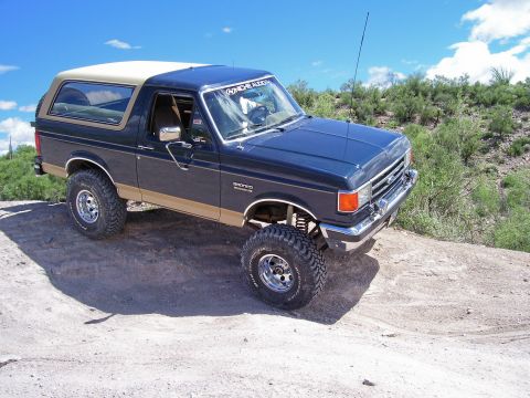 1991 Ford Bronco - This lifted 1991 Ford Bronco is shown off-roading on a sunny day with a clear blue sky.