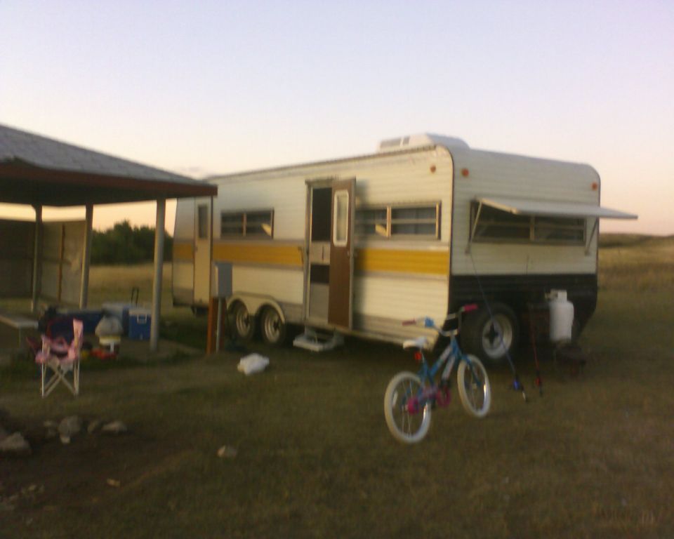 Camper trailer with yellow stripe, propane tank, and bicycle parked outside under a covered area