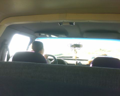 1989 Ford Bronco - View from the back seat of a vehicle shows a person driving, with the road visible through the windshield.
