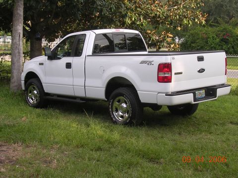 2006 Ford F-150 - A white 2006 Ford F-150 STX 4x4 pickup truck is parked on a grassy area with trees in the background.