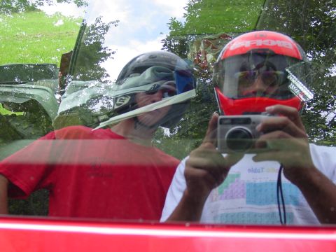 1998 Ford Mustang - Two individuals in helmets capture a selfie inside a red vehicle, with reflections of the outdoors visible.