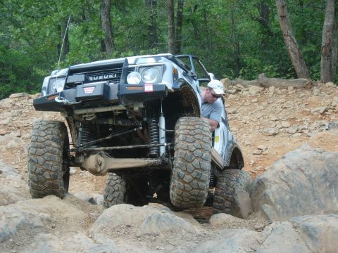 1995 Ford Bronco - A modified Suzuki Samurai navigates a rocky off-road trail with a driver assisting.